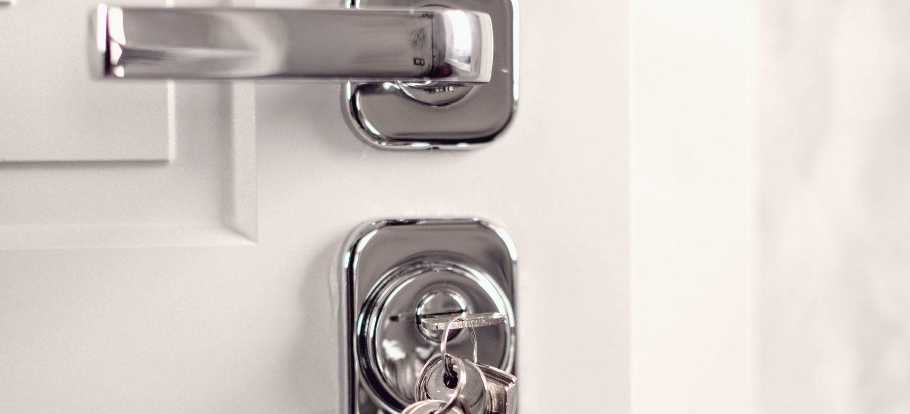 A chrome lever handle on a white door with a bunch of keys still hanging from the key in the cylinder below it.