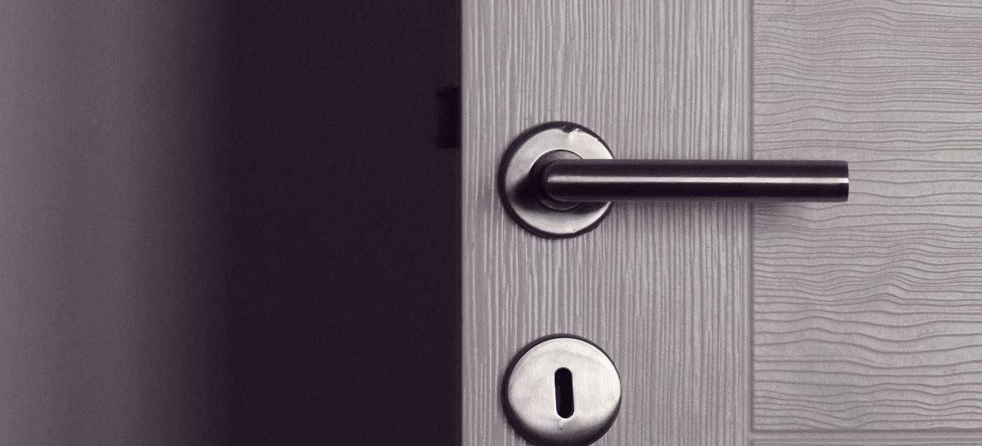 A lever handle and a separate keyhole escutcheon on a grey panelled door, photographed close and from the side.