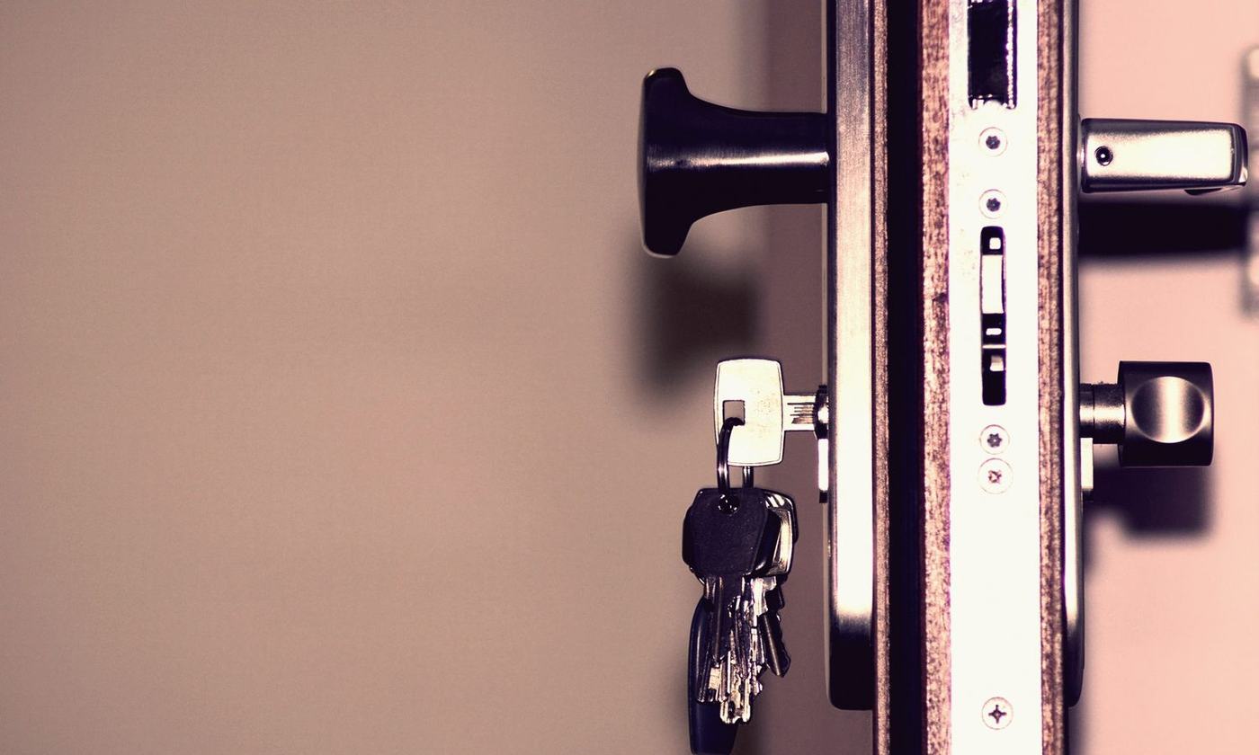 A bunch of keys hanging from the key in a door lock.